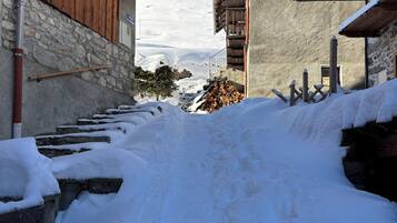 Un sentier enneigé mène à un bâtiment aux murs de pierre et aux balcons en bois.