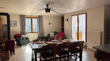 Un salon chaleureux avec une table à manger dressée pour quatre personnes, une cheminée et une grande fenêtre agrémentée de rideaux.