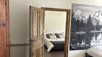 Une chambre avec une porte en bois, un lit avec une literie blanche, un radiateur et un tableau représentant un paysage de montagne accroché au mur.