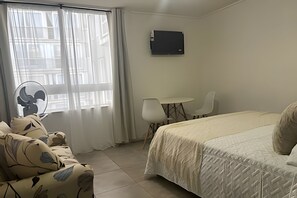 A hotel room with a bed, a desk, a chair, and a fan. - Estudio Amelia (Santiago)