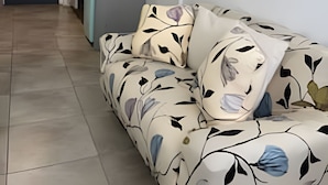 Ein Wohnzimmer mit einer Couch, einer Küchenzeile mit Schränken und einer Arbeitsplatte sowie einer Tür zu einem weiteren Raum.