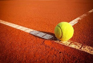 A tennis ball on a clay court with white boundary lines.