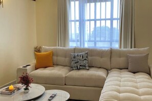 A living room with a beige sofa, a round coffee table, and a window with curtains. - Airport view Utawala 2 bdr (near JKIA)@0703500856 (Nairobi County)