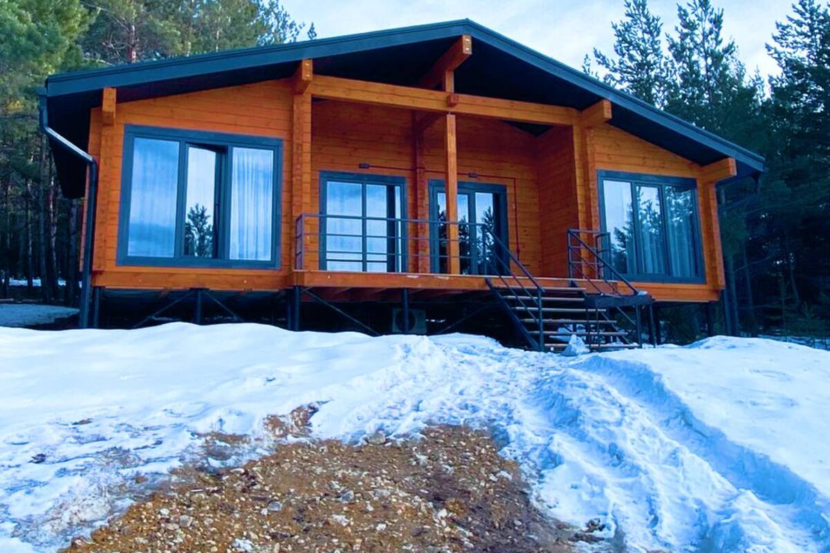 A wooden cabin with large windows, a covered porch, and a staircase leading to the entrance.