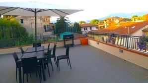 Une terrasse extérieure avec une table et des chaises, un barbecue et une vue sur les bâtiments et les montagnes environnants.