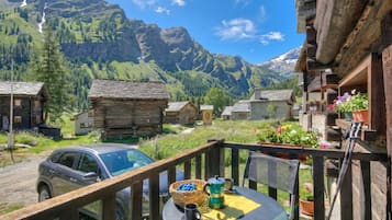 A wooden deck with a table, chairs, and a car parked outside.
