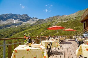 A terrace with tables and chairs, a wooden deck, and a mountainous backdrop. - Rustico Al Museo Bosco Gurin for 6 (Bosco Gurin)