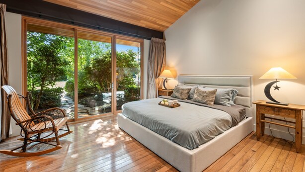 Une chambre moderne avec un grand lit, un plancher en bois et une vue sur la verdure grâce à de grandes portes coulissantes en verre.
