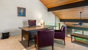 Une salle de réunion moderne avec une table en verre, des fauteuils en cuir, un plafond en bois et un portrait encadré accroché au mur.