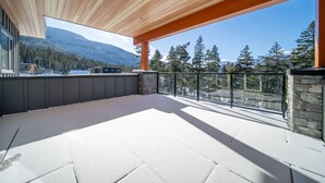 A spacious balcony with a wooden ceiling, stone walls, and a view of mountains and trees.