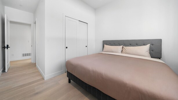 A bedroom with a large bed, a grey headboard, and white walls.