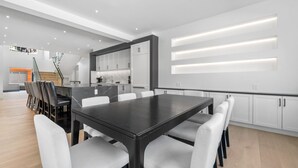 A modern kitchen with white cabinets, a dark wooden table, and white chairs.