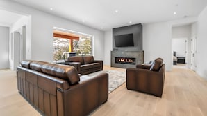 A spacious living room with a fireplace, leather sofas, and a flat-screen TV mounted on the wall.