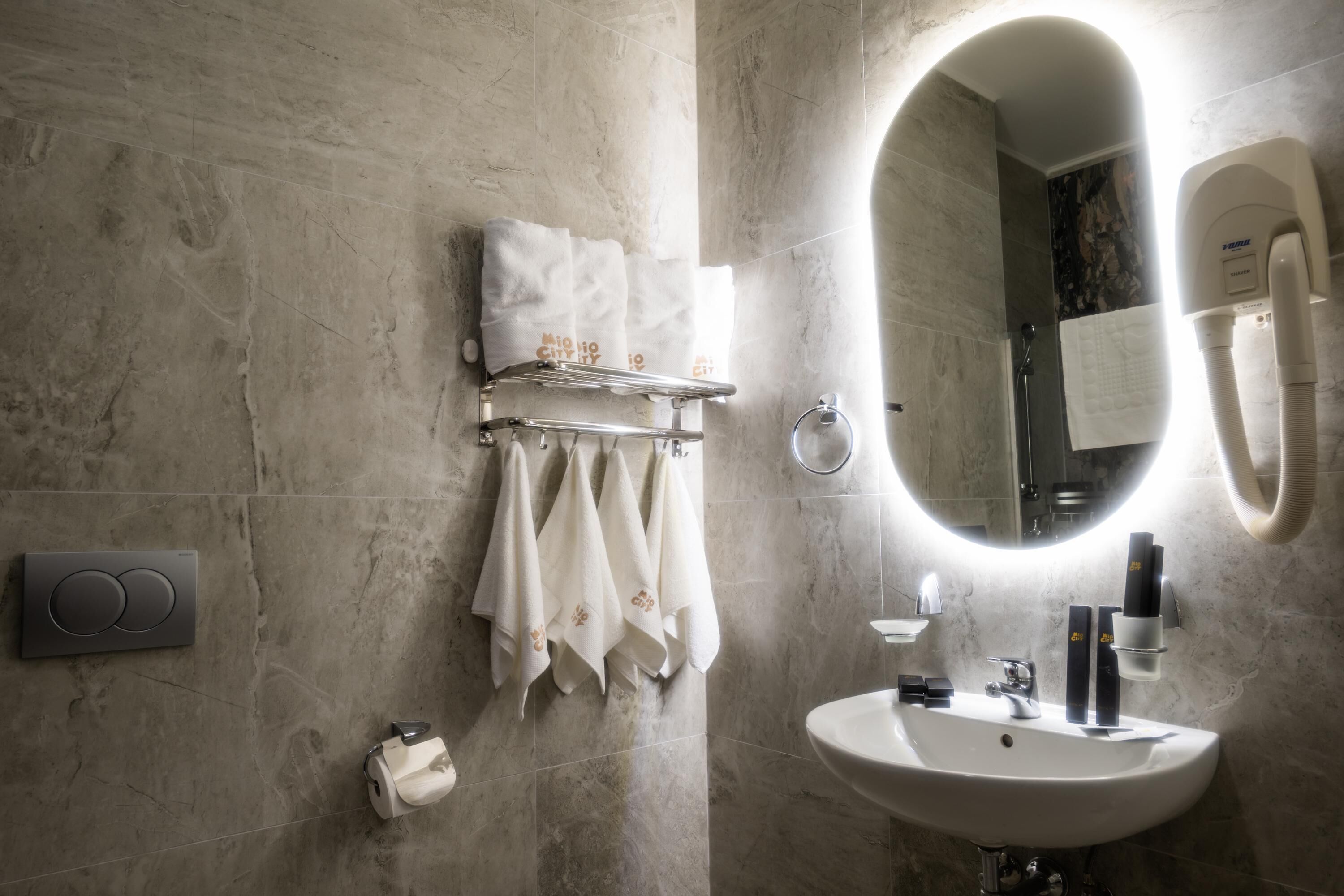 Un baño moderno con pared de mármol, un espejo grande, un lavabo y un perchero con toallas ordenadas.