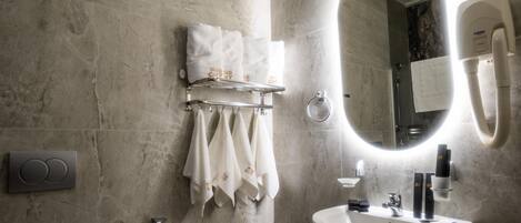Un baño moderno con pared de mármol, un espejo grande, un lavabo y un perchero con toallas ordenadas.