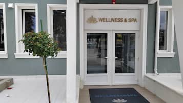 A building entrance with a sign reading 'WELLNESS & SPA' and a doormat with 'WELLNESS & SPA' and 'Mio City' text.
