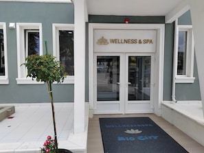 Entrada de un edificio con un letrero que dice 'WELLNESS & SPA' y un felpudo con los textos 'WELLNESS & SPA' y 'Mio City'.