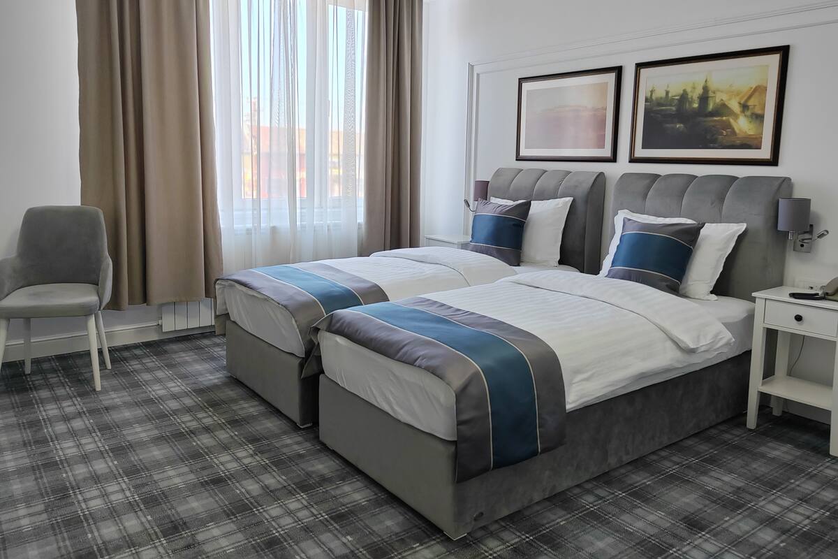 Une chambre d’hôtel avec deux lits, une chaise, une table de chevet et une fenêtre avec des rideaux.