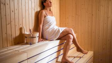 Une personne assise sur un banc en bois dans un sauna, avec un mur en bois et un seau.