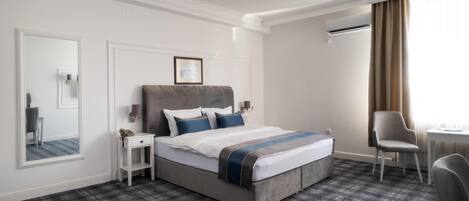 A hotel room with a large bed, a bedside table, a chair, a mirror, and a window with curtains.