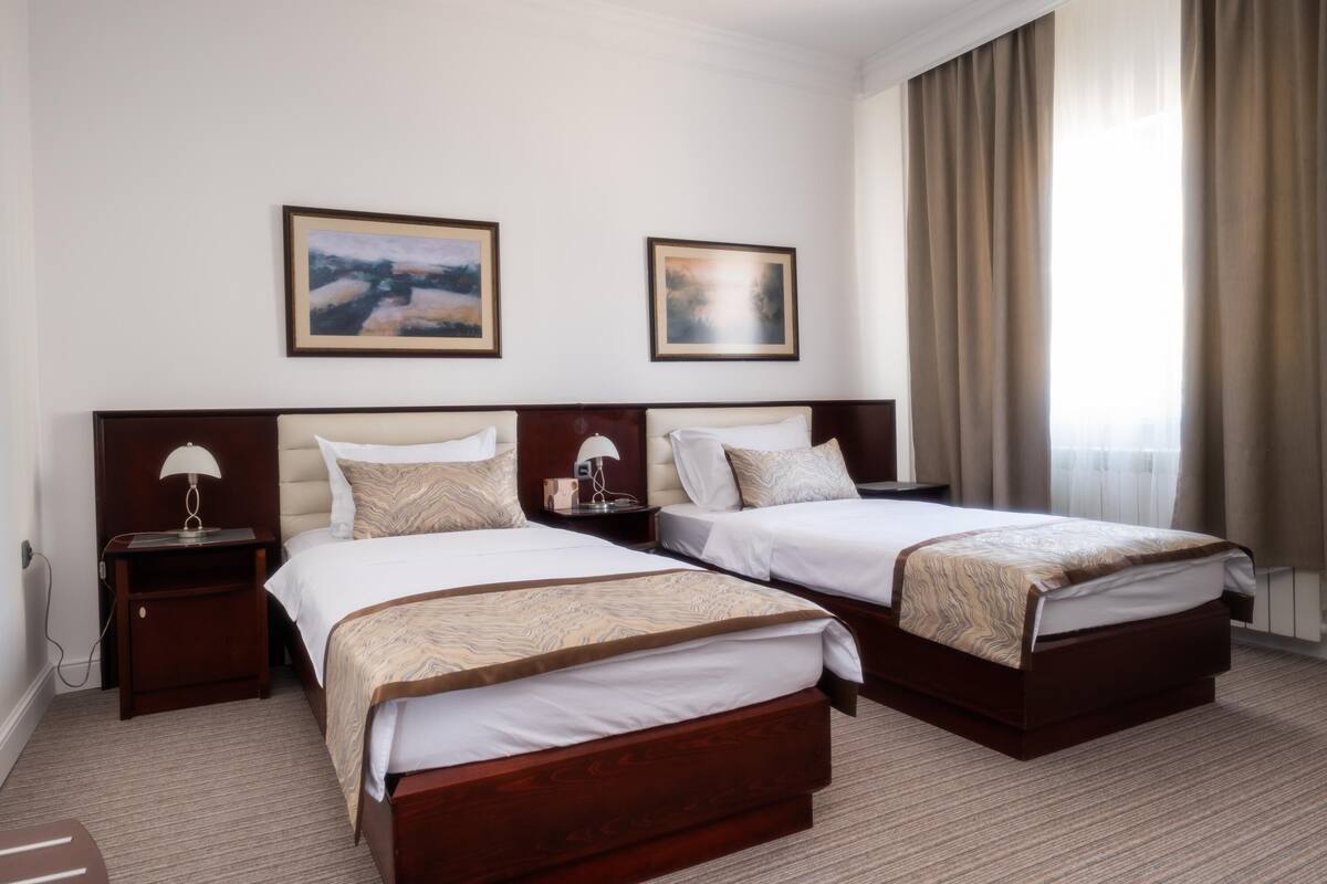Une chambre d’hôtel avec deux lits, une table de chevet avec une lampe et deux tableaux encadrés au mur.