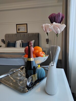Un plateau avec une bouteille de vin, des verres, un saladier de fruits et un vase de fleurs, posé sur une table dans une chambre d’hôtel.