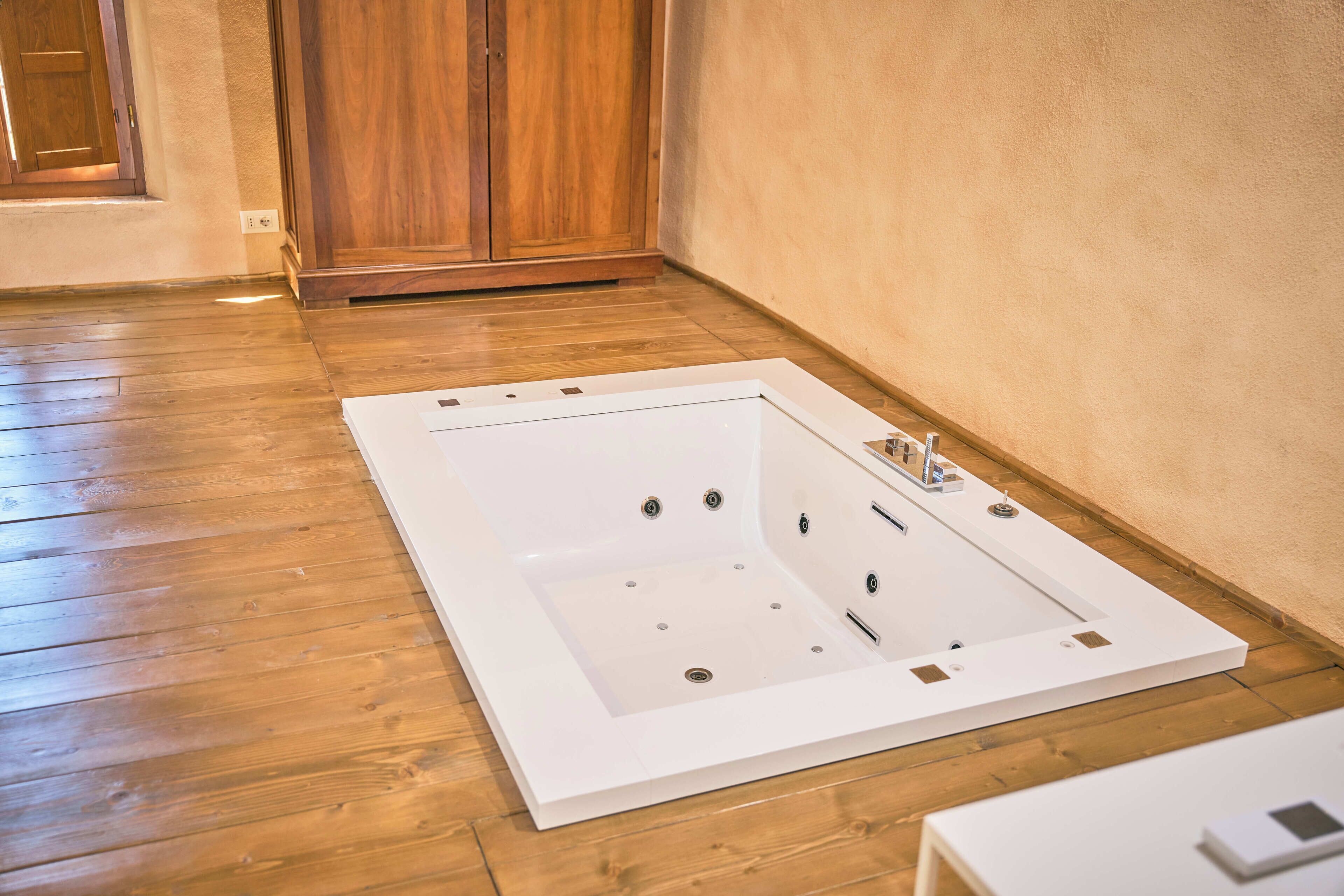 Una banyera gran i buida en una habitació amb terres de fusta i un armari de fusta.