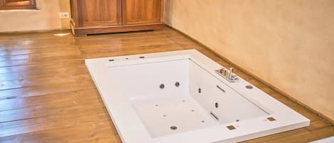 Una bañera grande y vacía en una habitación con suelo de madera y un armario de madera.