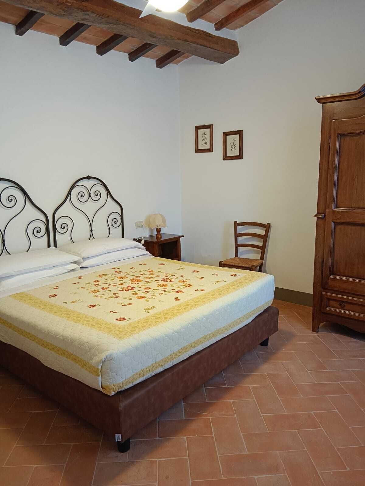 A bedroom with a bed, wooden headboard, a nightstand with a lamp, a chair, and a wardrobe.