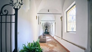 A corridor with a potted plant, a sofa, and a window with a metal grille. - Sant'Anna in Camprena Agriturismo (Pienza)