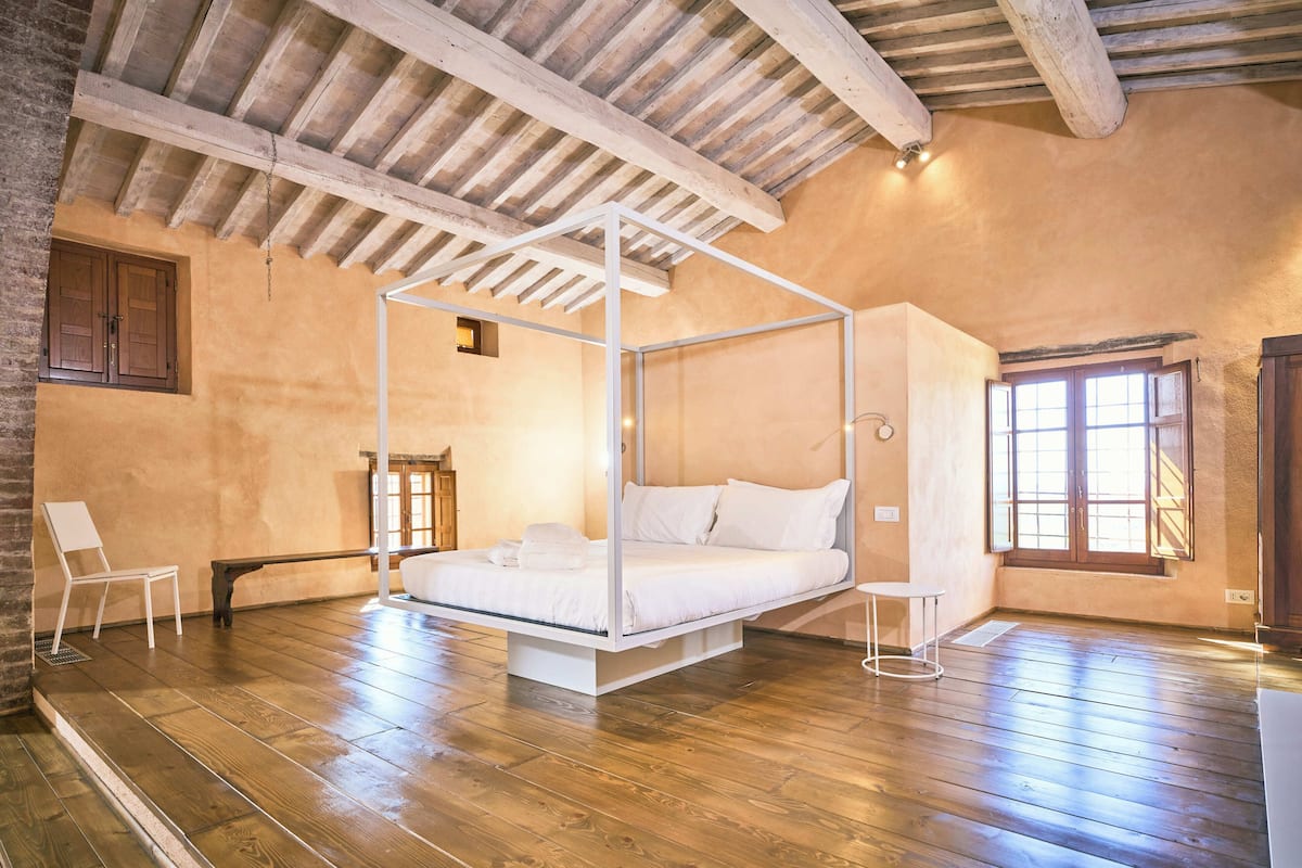 A room with a four-poster bed, wooden flooring, and a sloped ceiling with exposed beams.