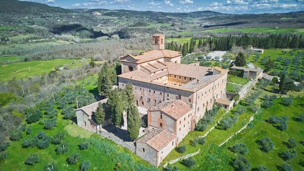 A large, historic stone building with multiple wings and a central tower, surrounded by lush green fields and trees. - Sant'Anna in Camprena Agriturismo (Pienza)