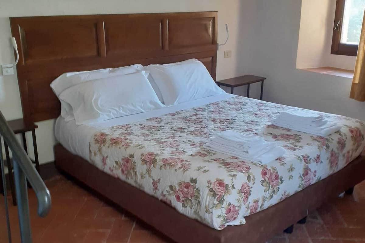 A bed with a floral bedspread, a wooden headboard, and a brick floor.