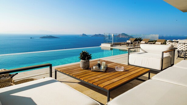 Ein Poolbereich mit Holztisch, weißen Liegestühlen und Blick auf das Meer.