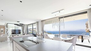 Eine moderne Küche mit einer großen Kochinsel, einem Essbereich mit Stühlen und Blick auf das Meer.
