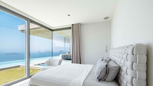 Ein modernes Schlafzimmer mit einem großen Bett, Meerblick und einer Glaswand.