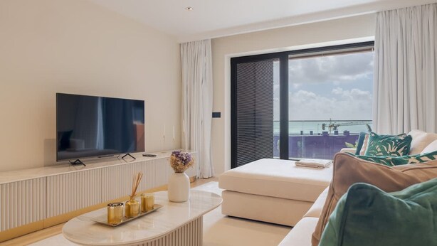 Una sala de estar moderna con un televisor de pantalla plana, un sofá blanco y una mesa de centro con objetos decorativos.