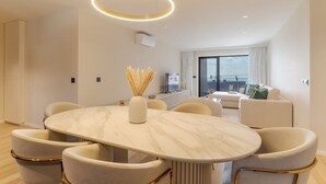 Un salón moderno con una mesa de comedor de mármol, sofás blancos y un ventanal con vista a la ciudad.