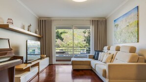 Sala de estar com piano, sofá, pintura e vista para o verde através de uma porta de correr.
