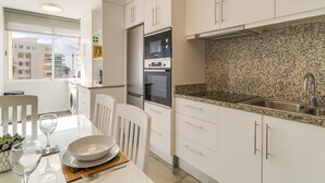 Cozinha moderna com armários brancos, bancada de granito e eletrodomésticos de aço inoxidável.