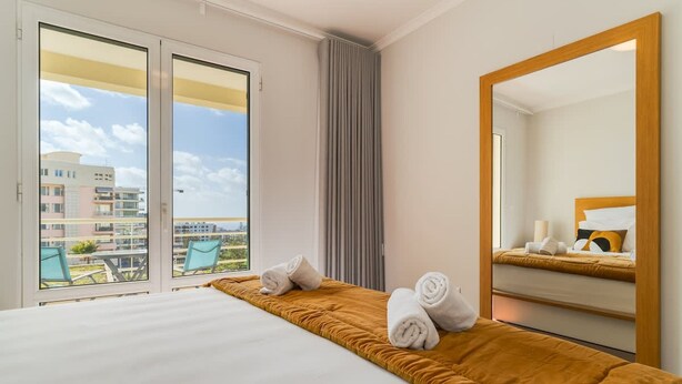 Quarto de hotel com uma cama, um espelho grande e vista para prédios pela janela.
