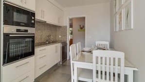 Cozinha moderna com armários brancos, forno Bosch e área de refeições com mesa e cadeiras brancas.