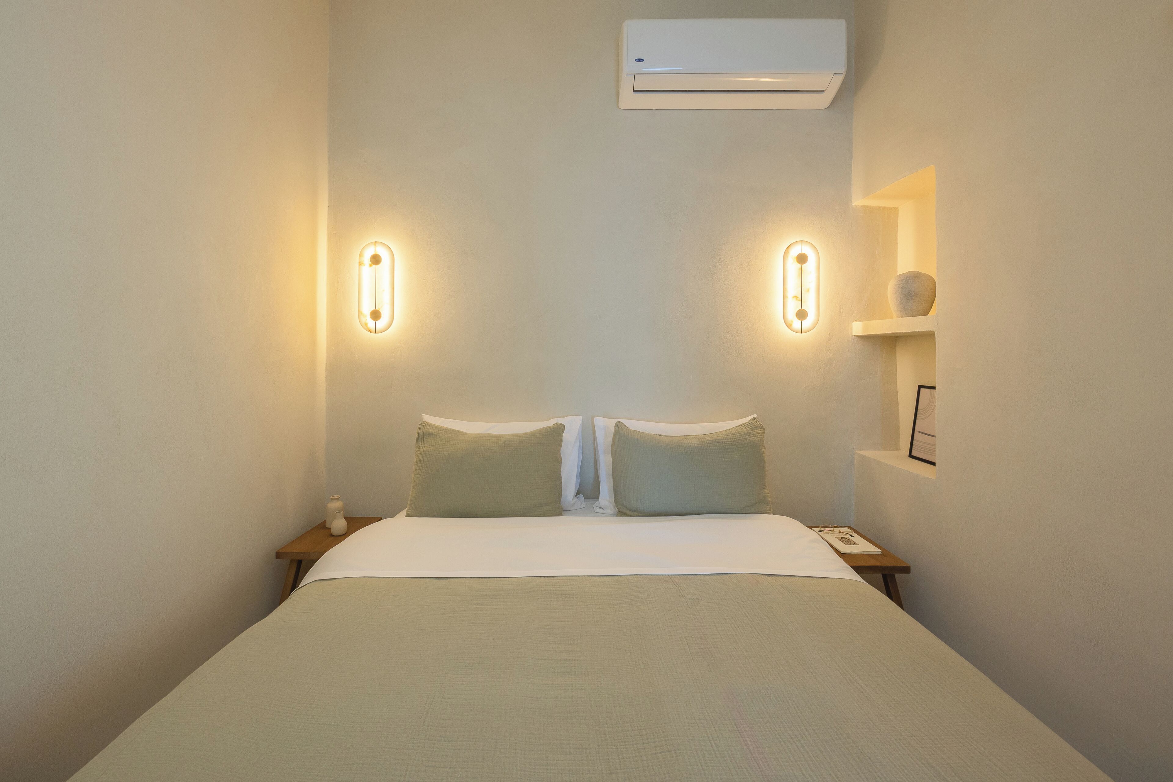 A neatly made bed with a white comforter and two pillows, flanked by bedside tables with a small vase and a framed picture.