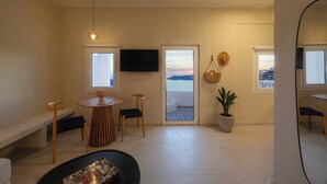 Un soggiorno moderno con TV, un'area pranzo con tavolo rotondo e vista sul mare attraverso una grande finestra.
