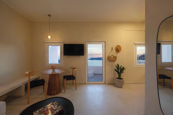 Een moderne woonkamer met een televisie, een eethoek met een ronde tafel, en uitzicht op zee door een groot raam.