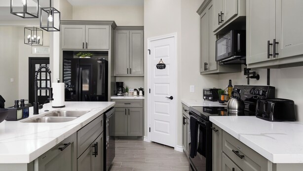A modern kitchen with grey cabinets, a white countertop, and a black stove. There is a white door with a hanging sign, and a black microwave above the stove.