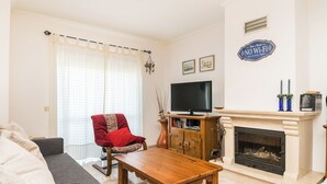 A living room with a sofa, a red armchair, a wooden coffee table, a television, a fireplace, and a 'No Wi-Fi' sign.