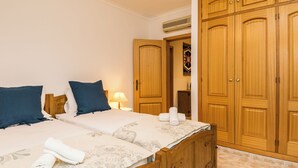 A bedroom with two beds, wooden wardrobes, and a bathroom visible through an open door.