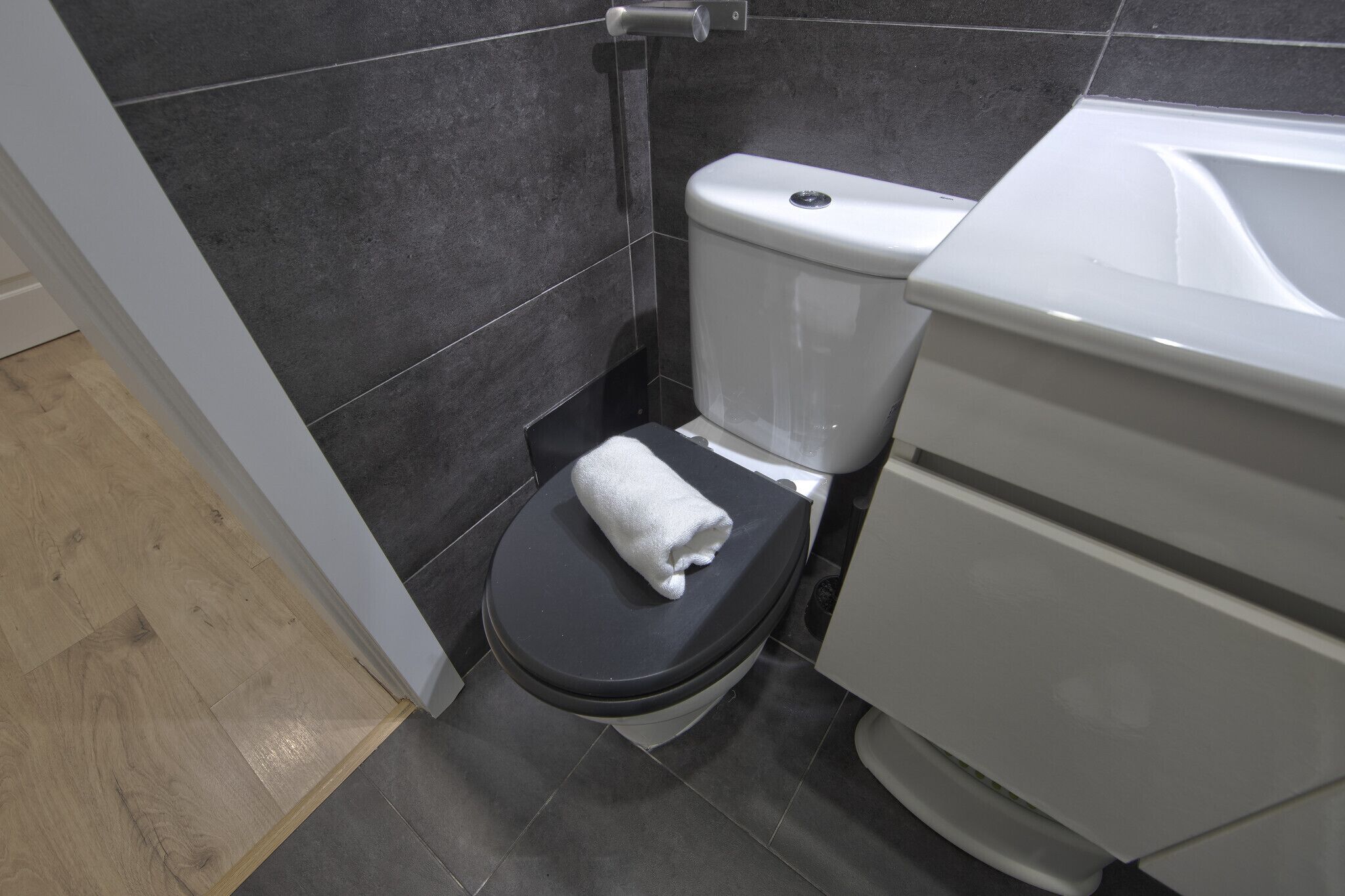 A modern bathroom with a black toilet, a white sink, and dark grey tiles.