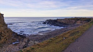 A coastal landscape with rocky cliffs, a pebbly beach, and a paved path along the shore. - The Beaches, beachfront 2 bed home with seaviews in Banff Aberdeenshire (Banff)